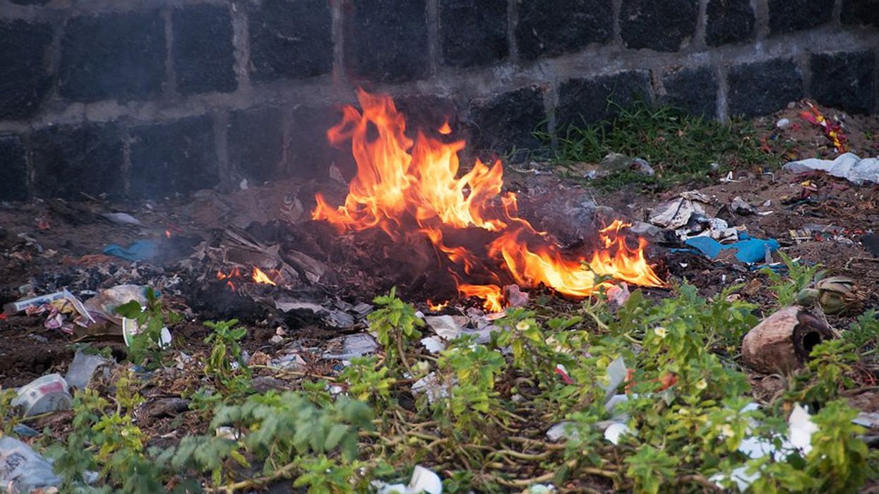 A small pile of burning plastic waste next to a brick wall.