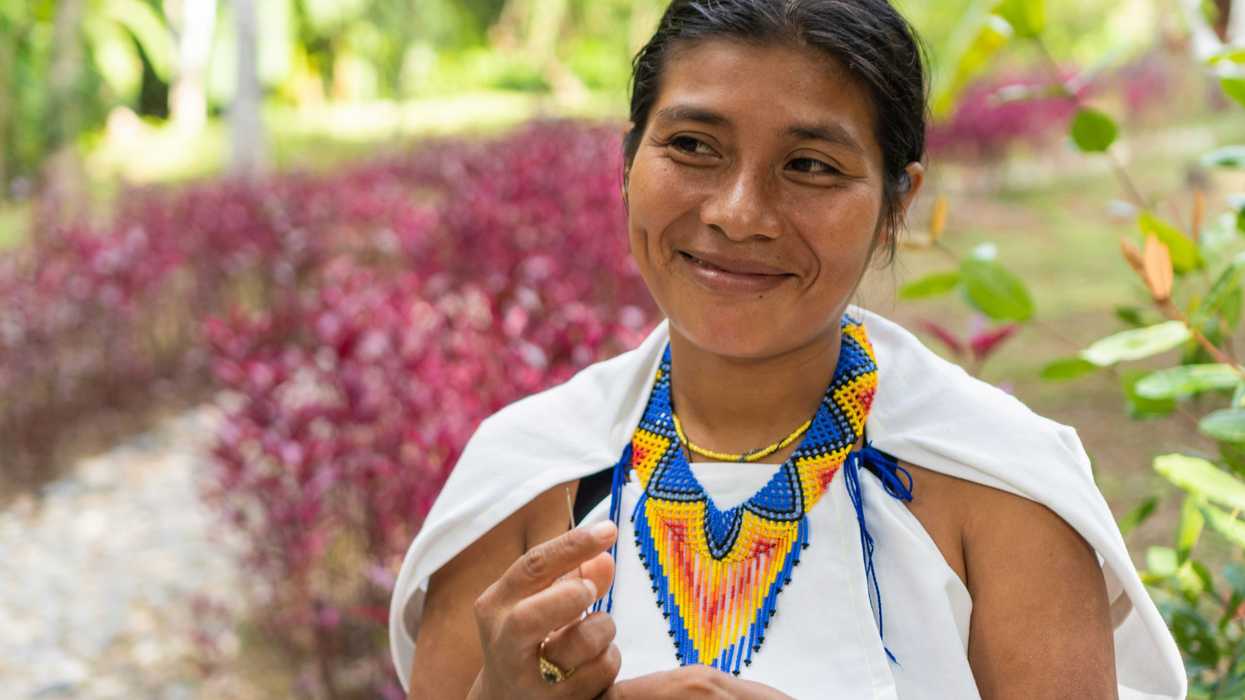 A smiling Indigenous woman wearing a colorful beaded necklace and white clothing.