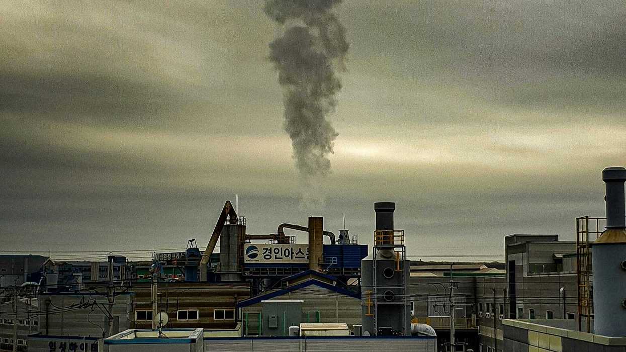 a smokestack billows from a building in a city.