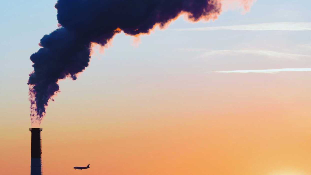 A smokestack silhouetted against a city skyline at sunset.