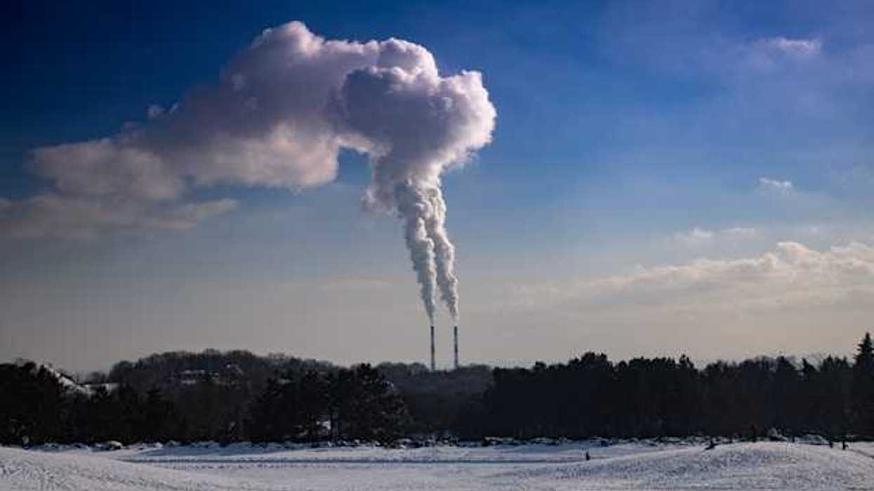 A snowy landscape with two smokestacks emitting pollution in the background