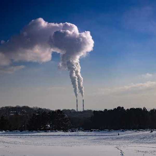 A snowy landscape with two smokestacks emitting pollution in the background