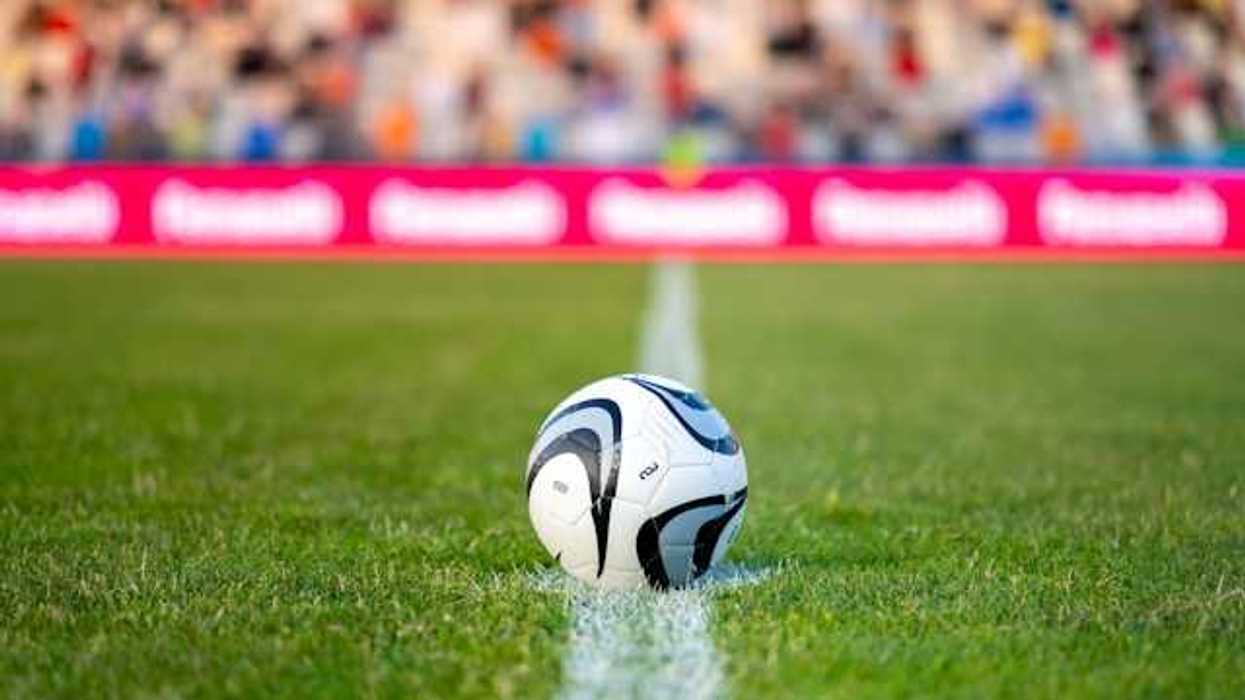 A soccer ball on green grass with people seated in bleachers in the background