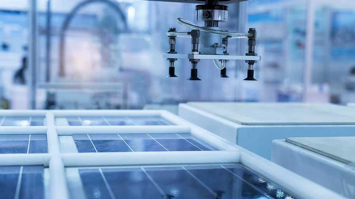 A solar panel in a manufacturing plant with a robotic arm hovering above it