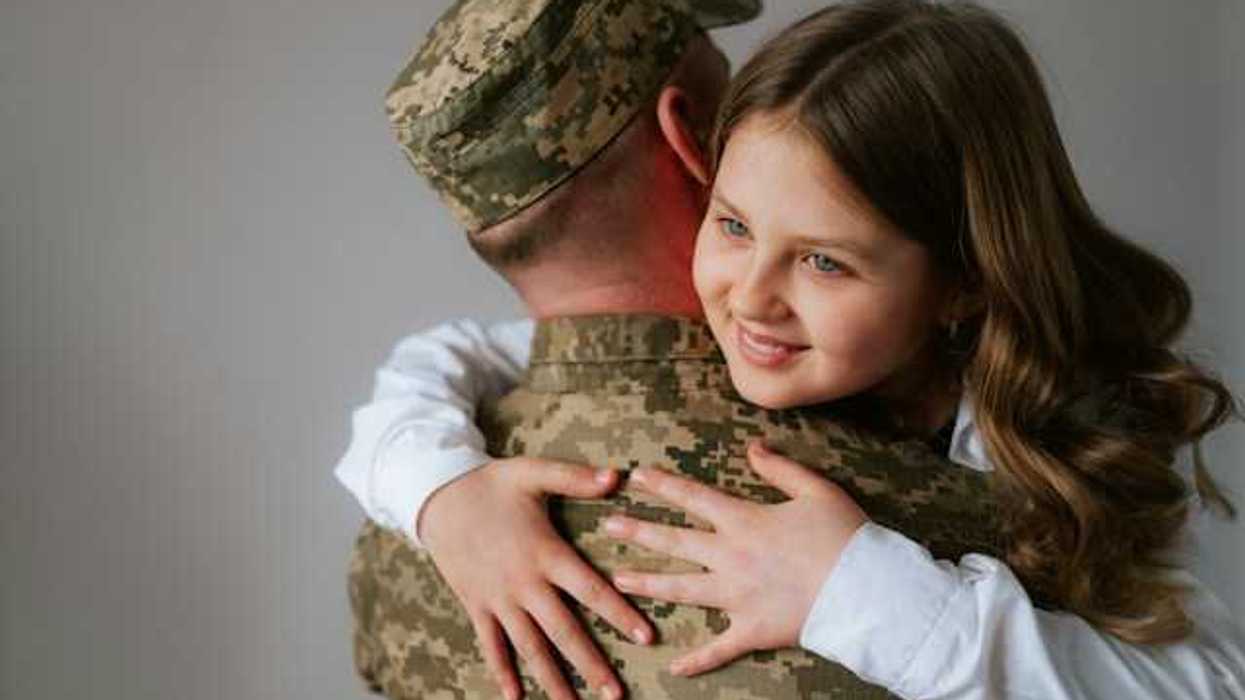 A soldier in fatigues hugging a young girl