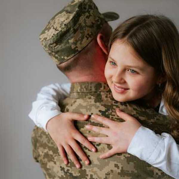A soldier in fatigues hugging a young girl