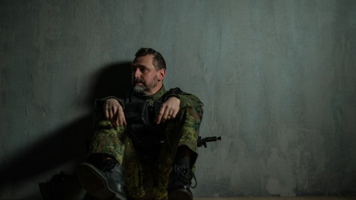 A soldier sitting on the floor leaning against a wall.
