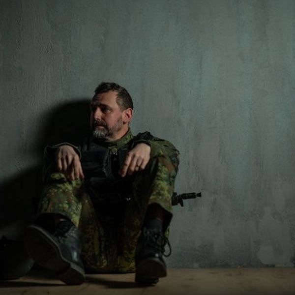 A soldier sitting on the floor leaning against a wall.