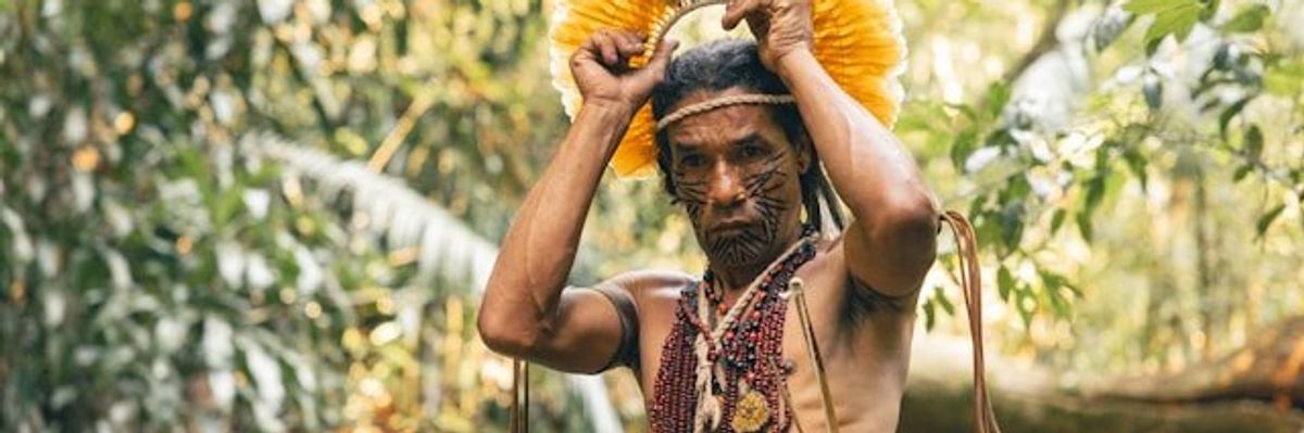 A South American indigenous man placing a headdress on his head.