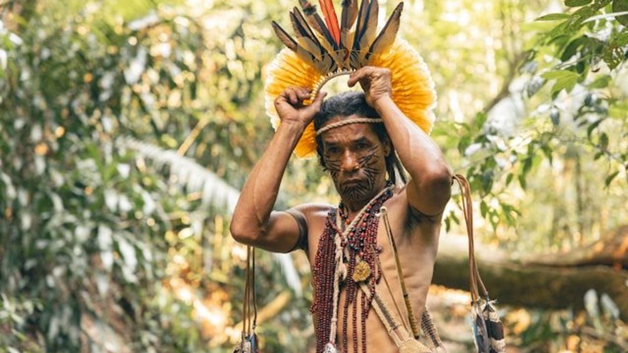 A South American indigenous man placing a headdress on his head.
