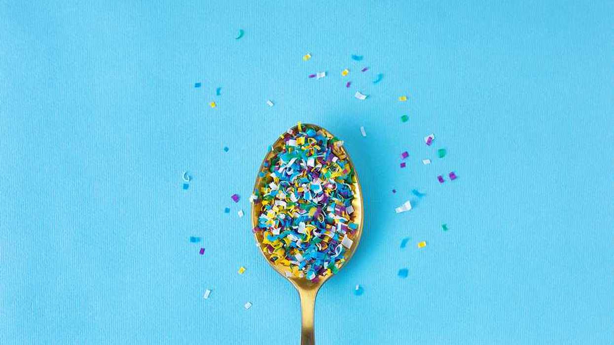 A spoon filled with tiny pieces of plastic sitting on a blue background