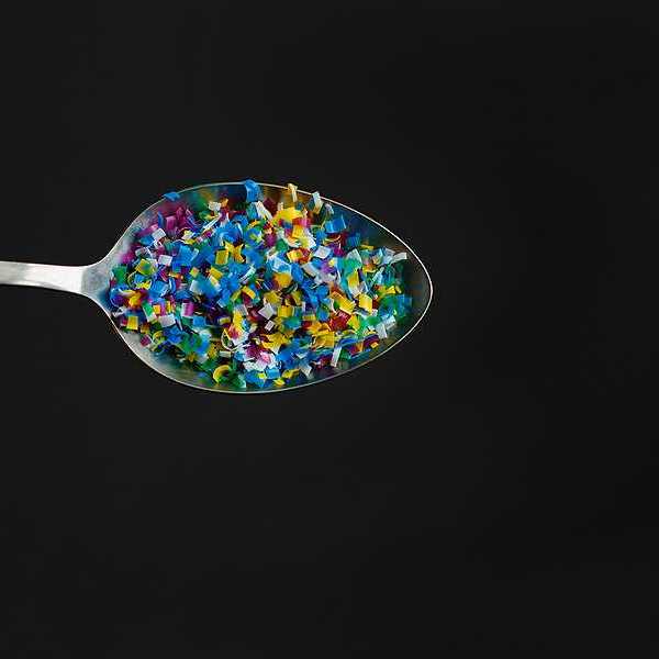 A spoon with small pieces of plastics in it against a black background