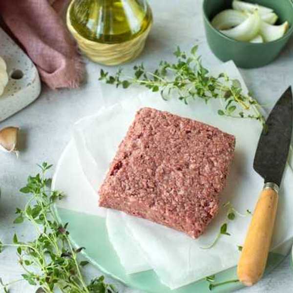 A square slab of real or vegan meat on a surface surrounded by spices