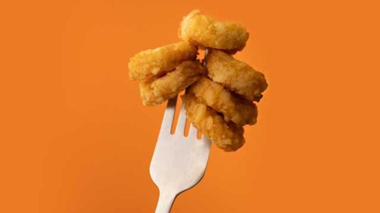 A stack of chicken mcnuggets speared on a fork against an orange background