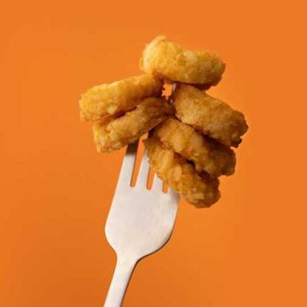 A stack of chicken mcnuggets speared on a fork against an orange background