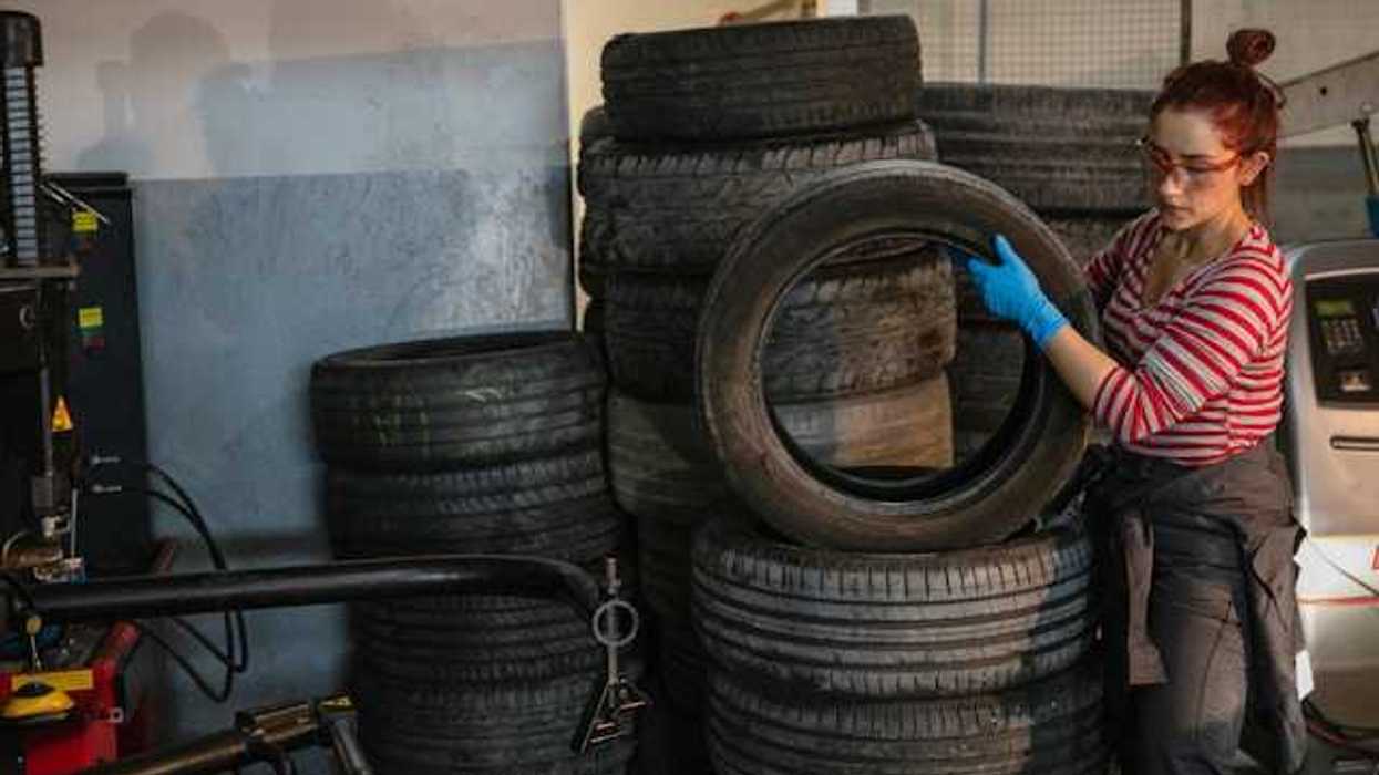 A stack of old tires being handled by a woman wearing a red and white striped shirt