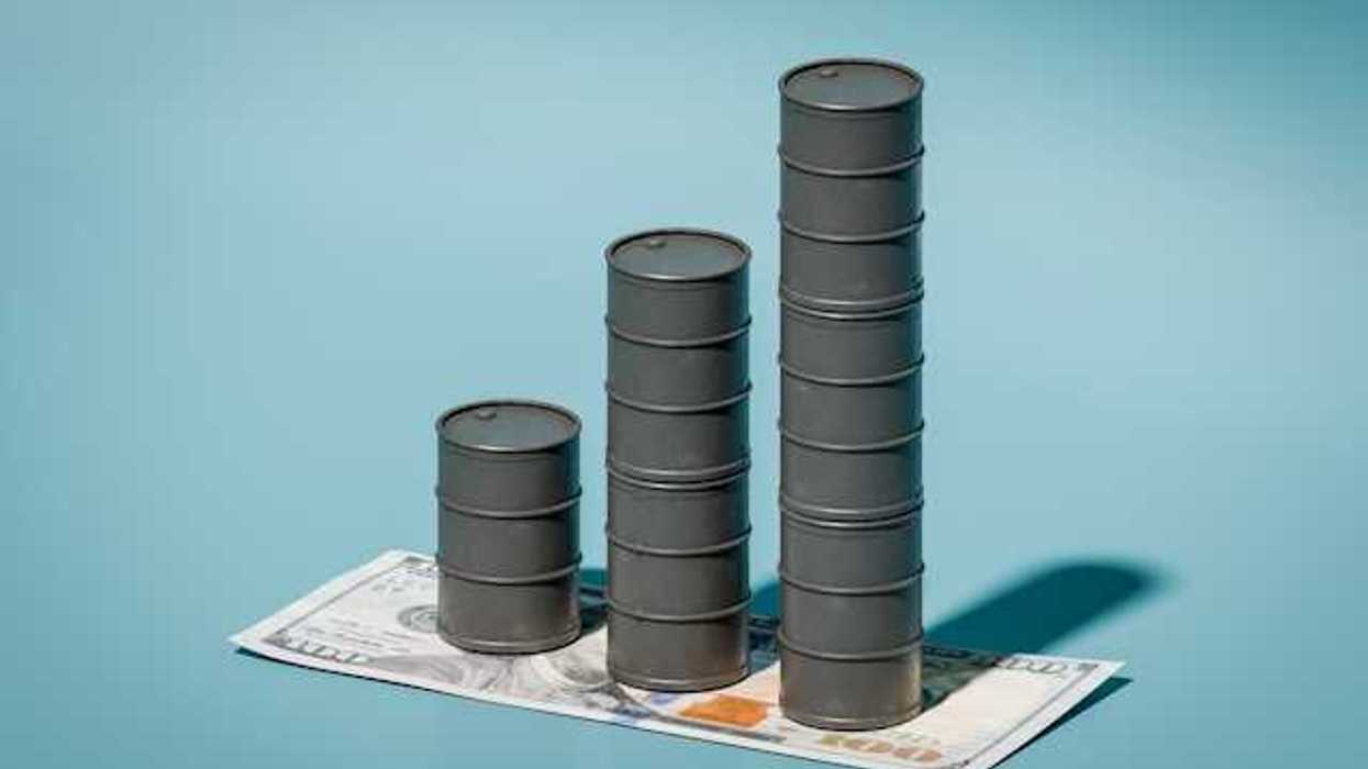A stack of three oil barrels on top of a one hundred dollar bill against a blue background