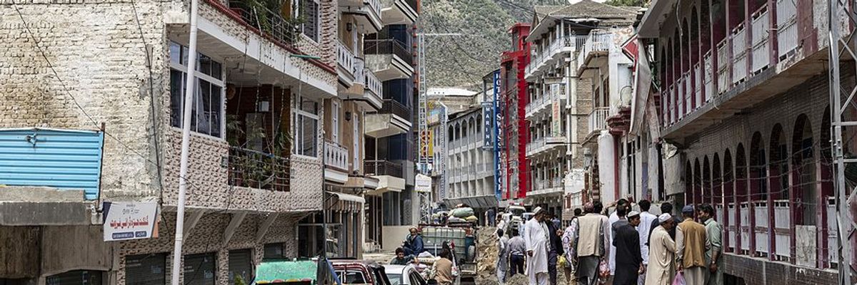 A street in Pakistan in the aftermath of a flood with people walking to one side and cars to the other.