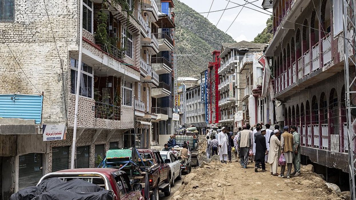 A street in Pakistan in the aftermath of a flood with people walking to one side and cars to the other.