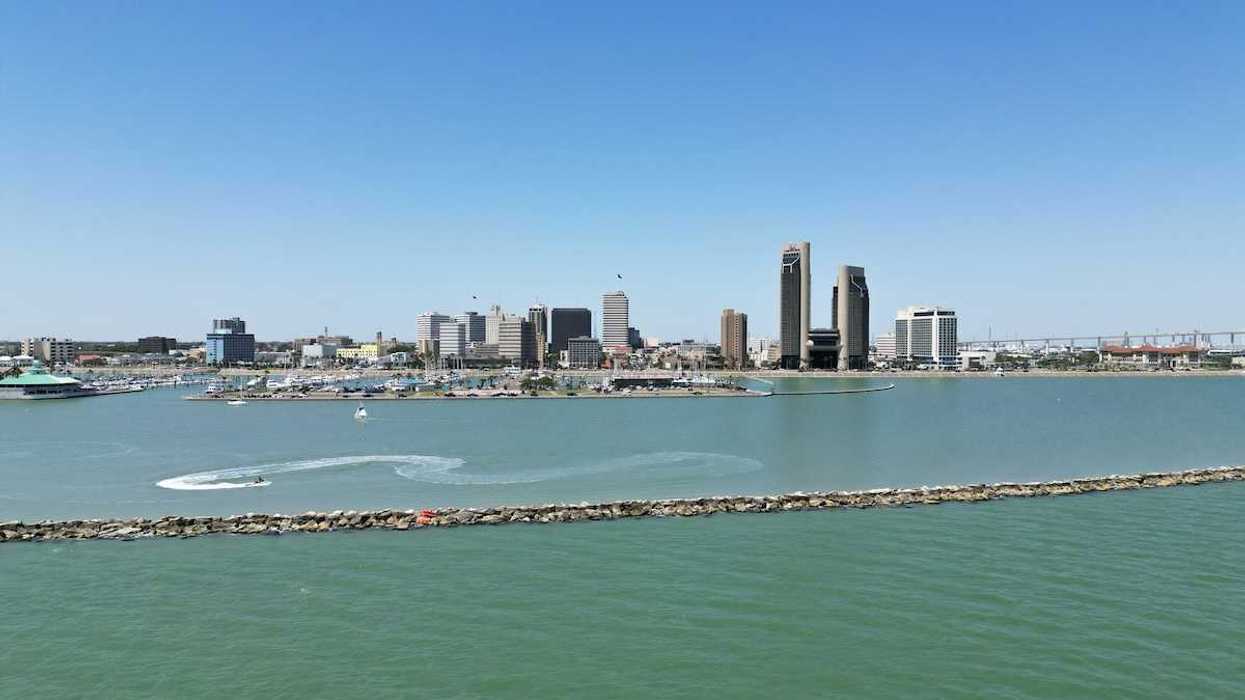 A sunny aerial view of downtown Corpus Christi, Texas, with the sparkling bay in the foreground and boats cruising through the water.