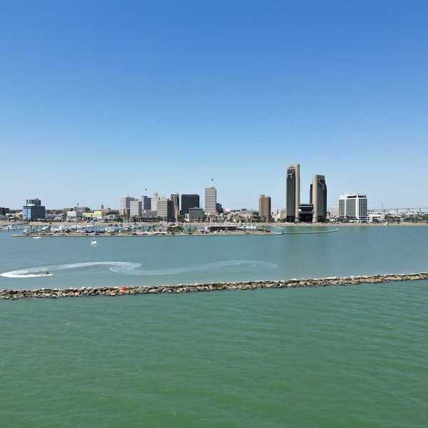 A sunny aerial view of downtown Corpus Christi, Texas, with the sparkling bay in the foreground and boats cruising through the water.