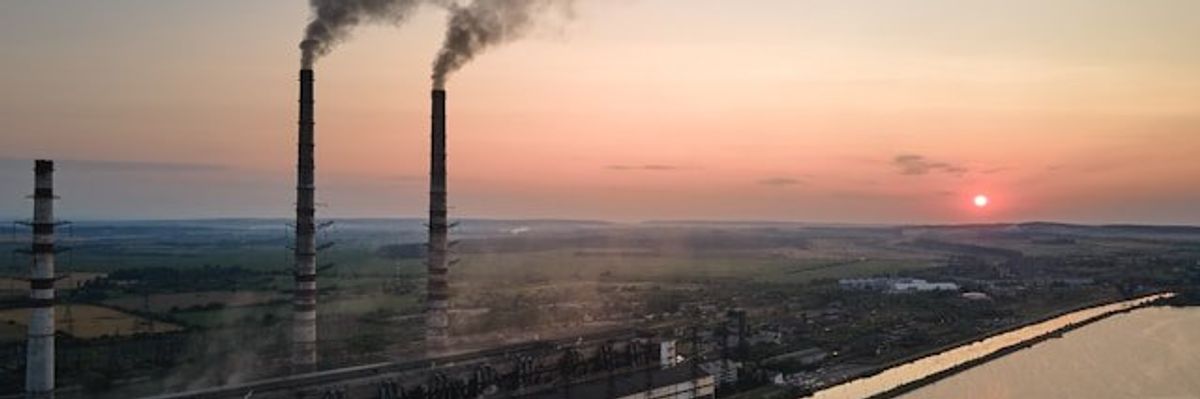 A sunset view of a factory with smokestacks billowing smoke.