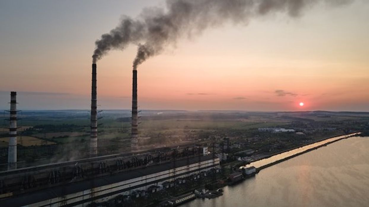 A sunset view of a factory with smokestacks billowing smoke.