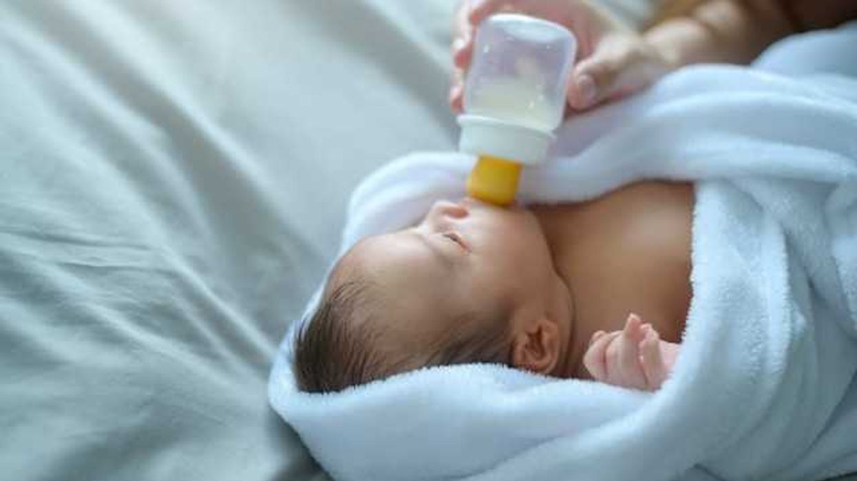 A swaddled baby being given a bottle