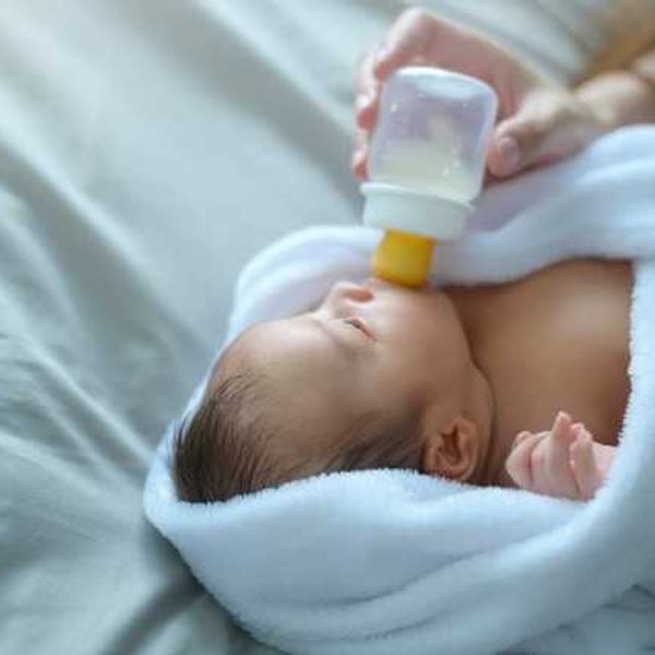 A swaddled baby being given a bottle