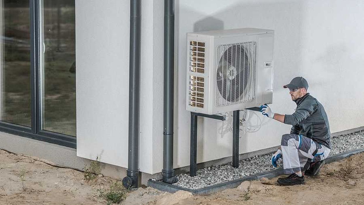 A technician working on a heat pump installed on the side of a home