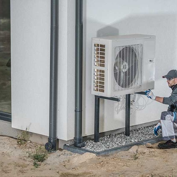 A technician working on a heat pump installed on the side of a home