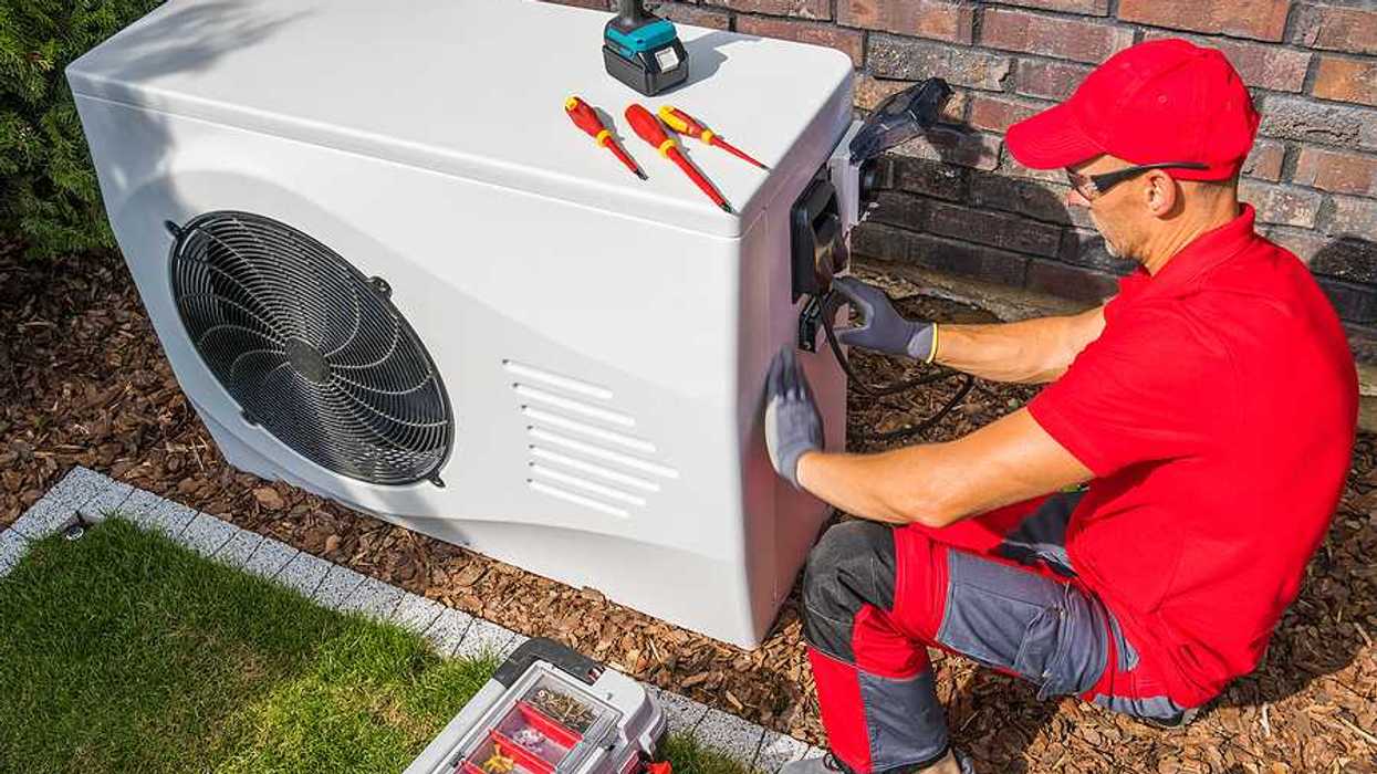 A technician working on a heat pump outside a house