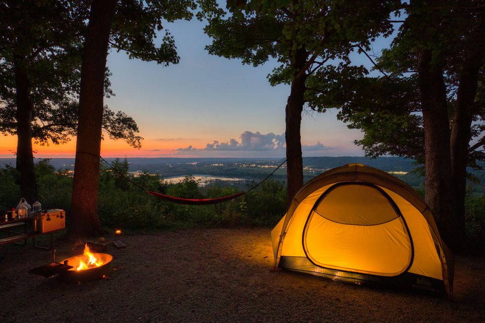 A tent and campfire with trees and sunset in background.
