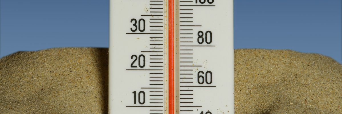 A thermometer in the sand showing temperatures near 40 degrees celsius with a blue sky in the background.