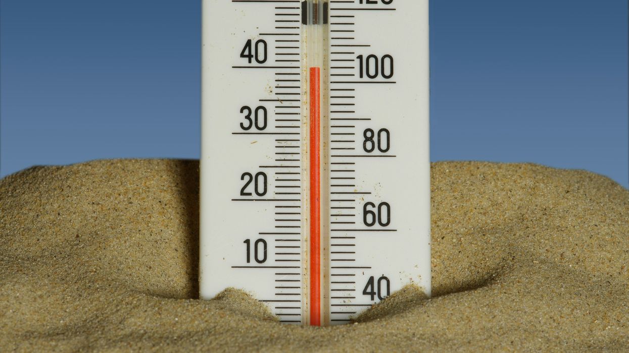 A thermometer in the sand showing temperatures near 40 degrees celsius with a blue sky in the background.