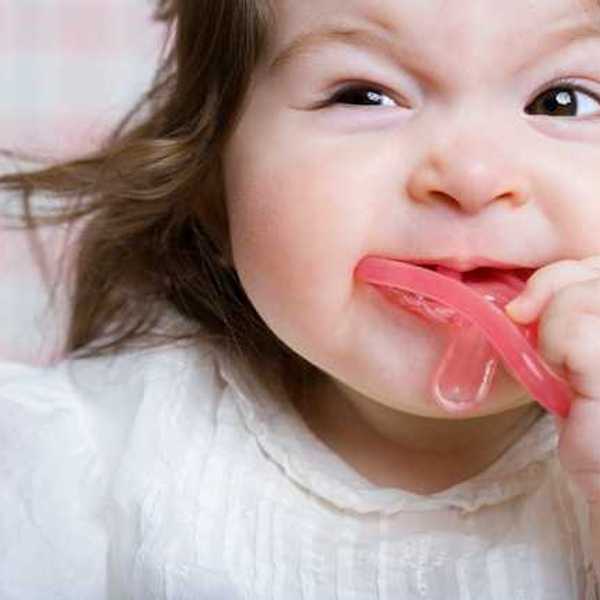 A toddler girl with a pink pacifier in her mouth