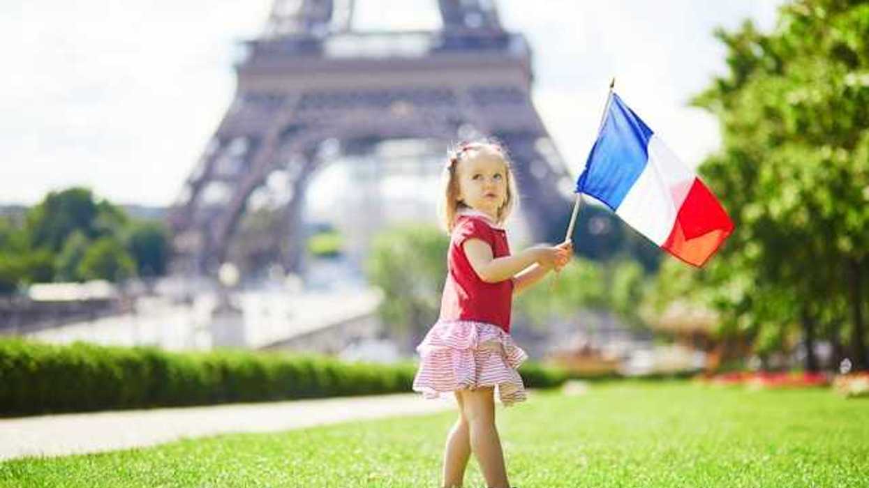 A toddler holding a French flag standing next to the Eiffel Tower in Paris