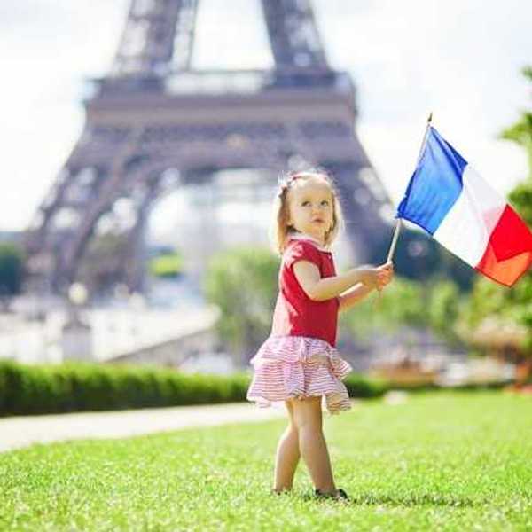 A toddler holding a French flag standing next to the Eiffel Tower in Paris