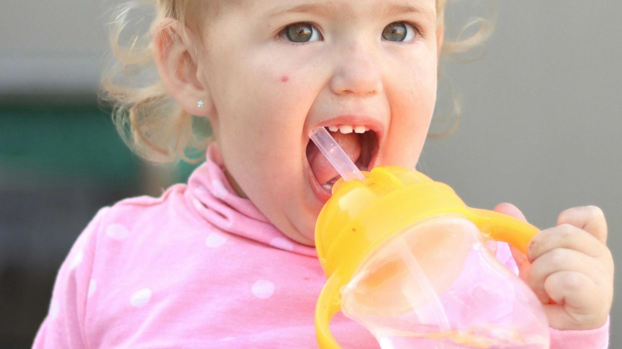 A toddler in a pink shirt drinking from a straw in a plastic sippy cup.