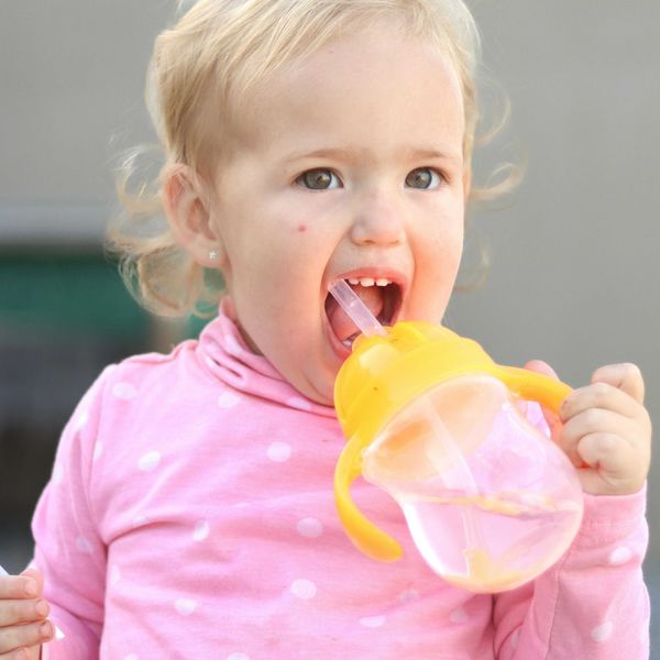 A toddler in a pink shirt drinking from a straw in a plastic sippy cup.