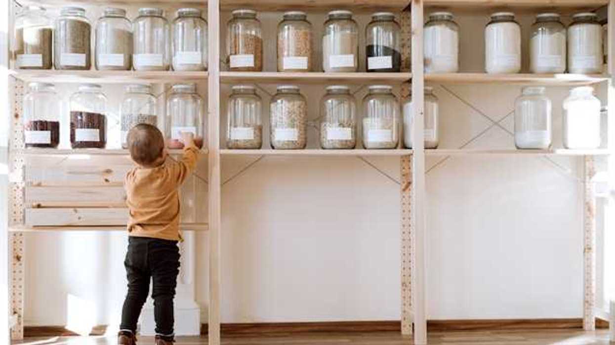 A toddler reaching up to a pantry shelf where jars of non perishable food is stored