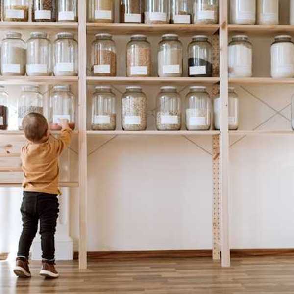 A toddler reaching up to a pantry shelf where jars of non perishable food is stored