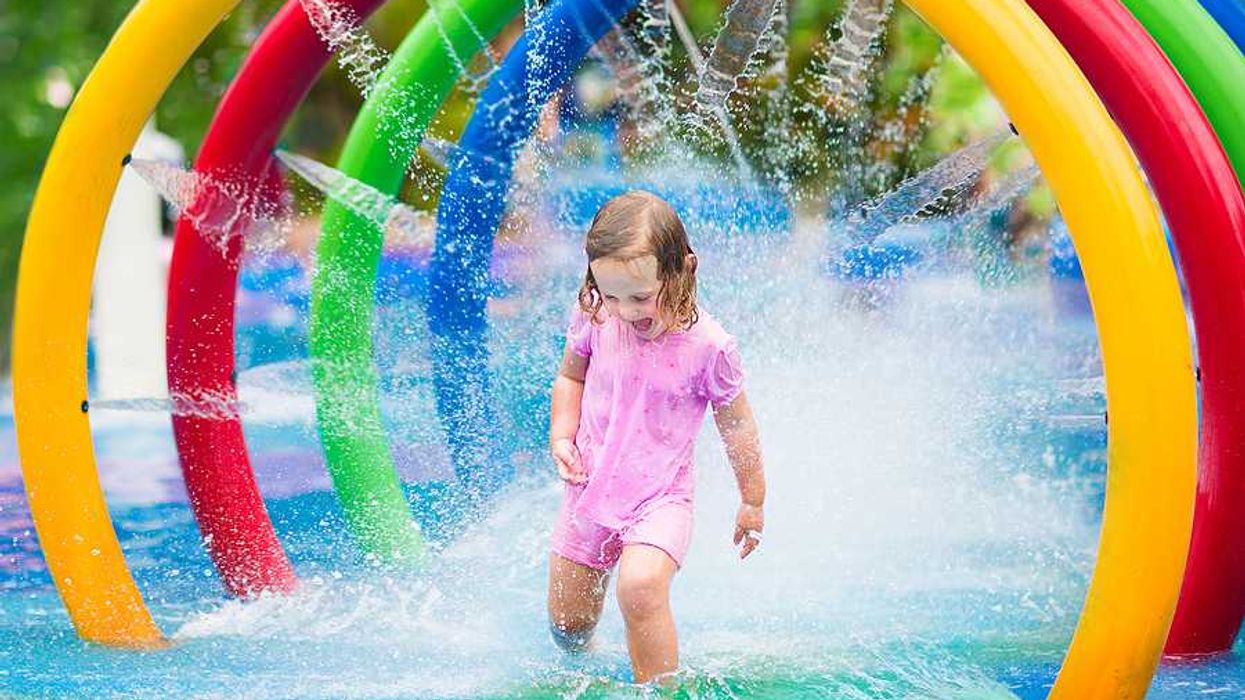 A toddler run through a multicolored fountain on a hot day