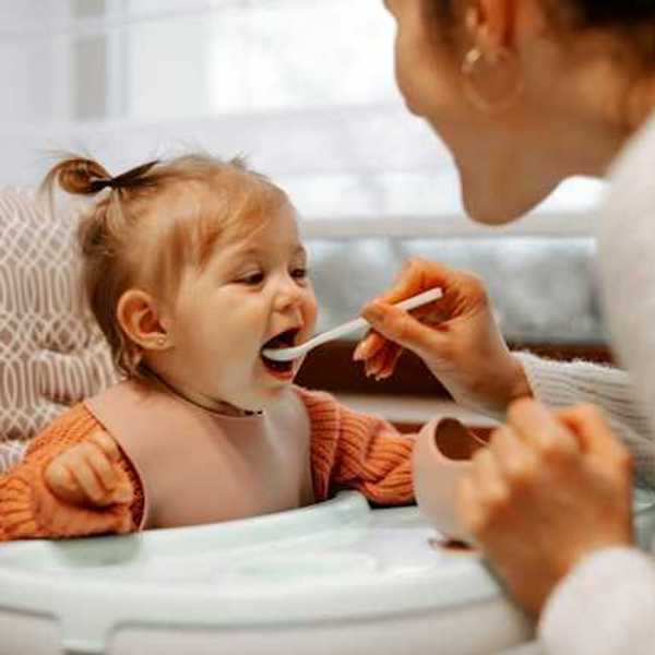 A toddler sitting in a high chair being fed by her mother