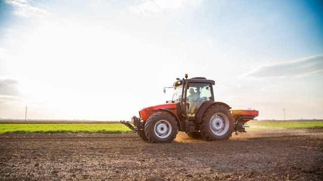 A tractor applying fertilizer on a brown field