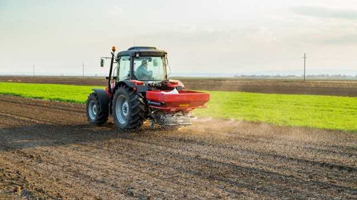 A tractor applying fertilizer to a brown farm field