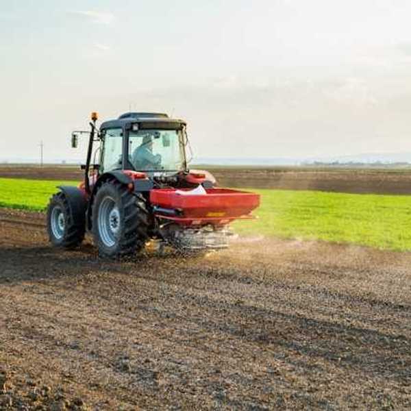 A tractor applying fertilizer to a brown farm field