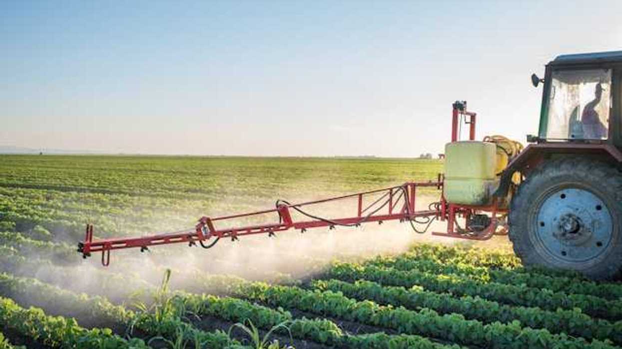A tractor applying pesticides to a green farm field