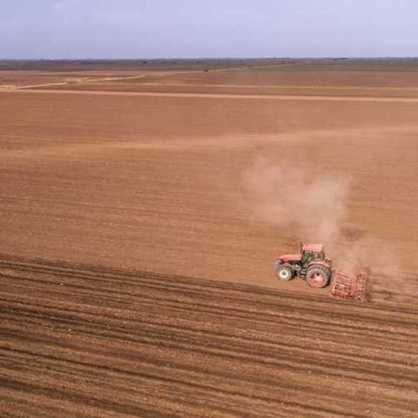 A tractor dragging an implement across a dry farm field
