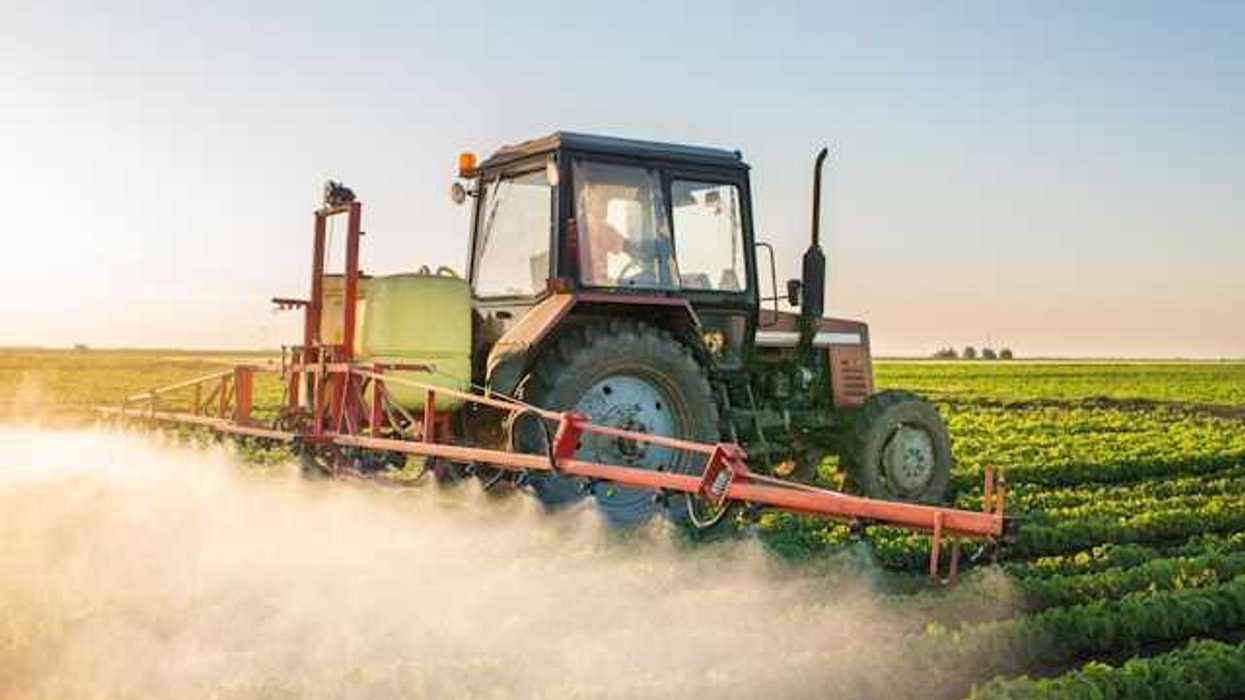 A tractor driving through a farm field applying pesticides